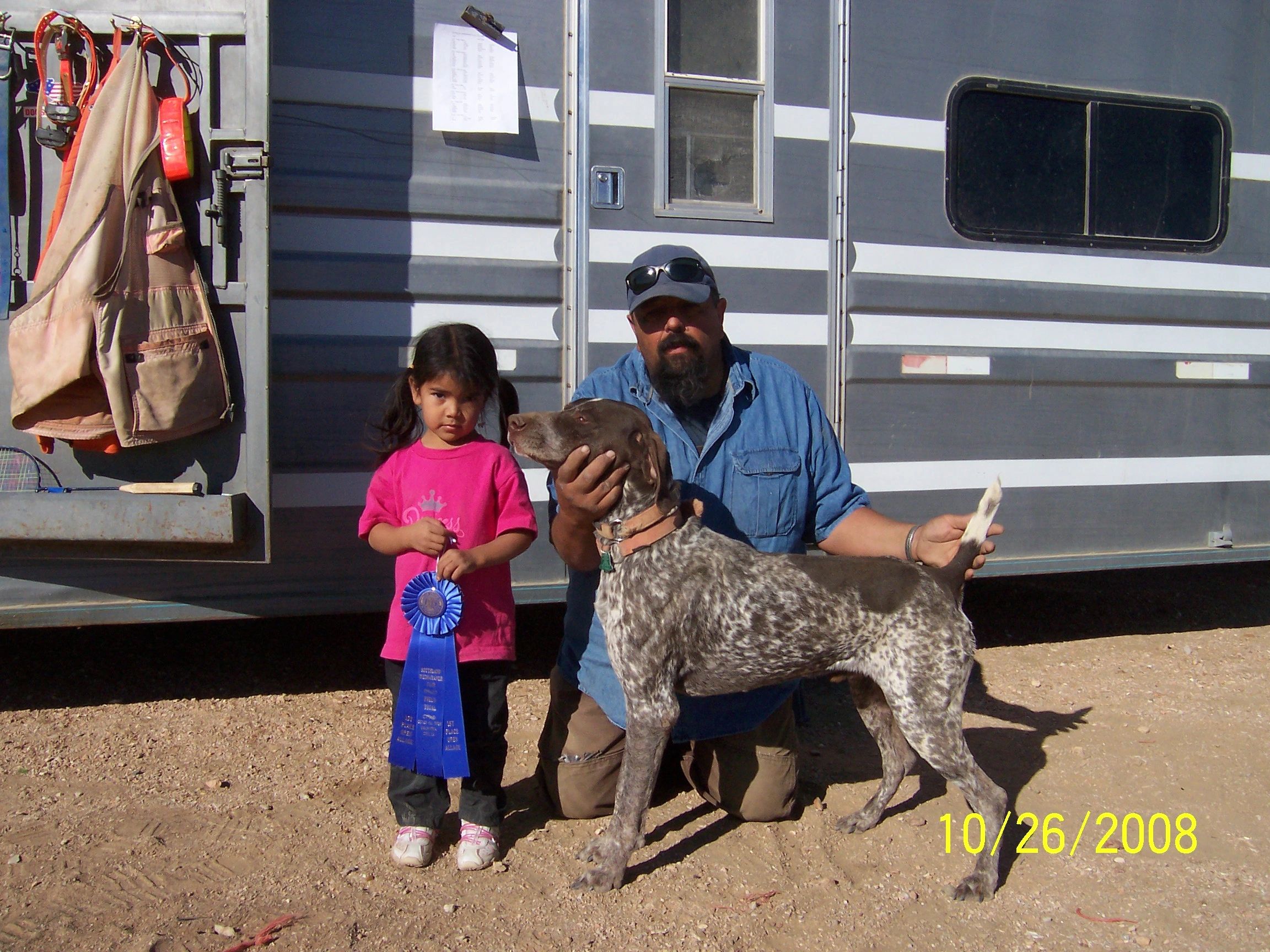 Man and girl with dog and blue ribbon outdoors